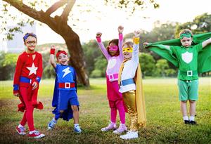5 kids dressed as superheroes two are raising arms straight in the air, one of them has there arms spread out holding a cape, one is making a fist, and the last one is wearing red  and walking
