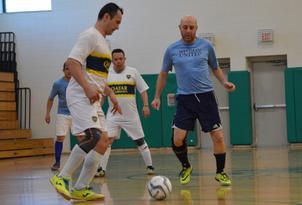 three men playing soccer in a gym with the ball in between two players