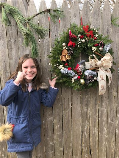 girl standing next to a wreath that is decorated for the christmas season